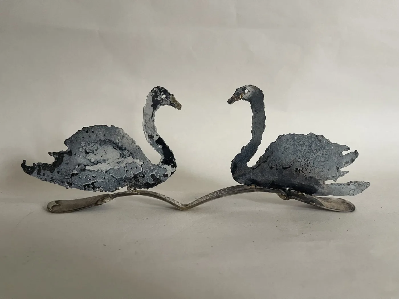 Two dark metal swan sculptures facing each other, joined at the base