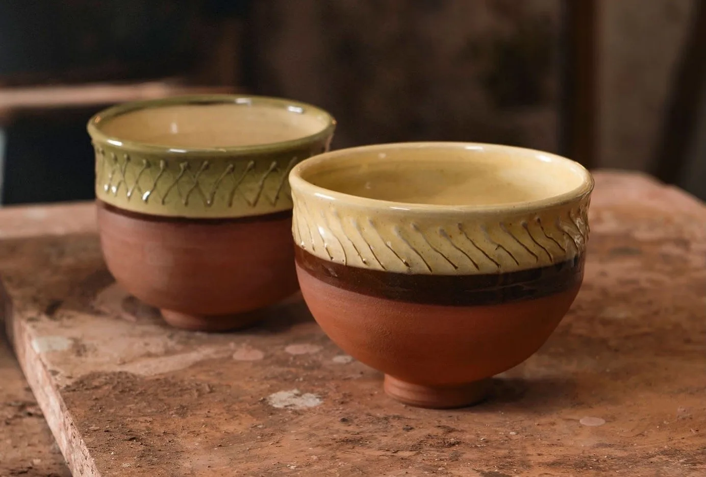 Two thrown pottery bowls with cream glazed rims and terracotta bases on a stone slab